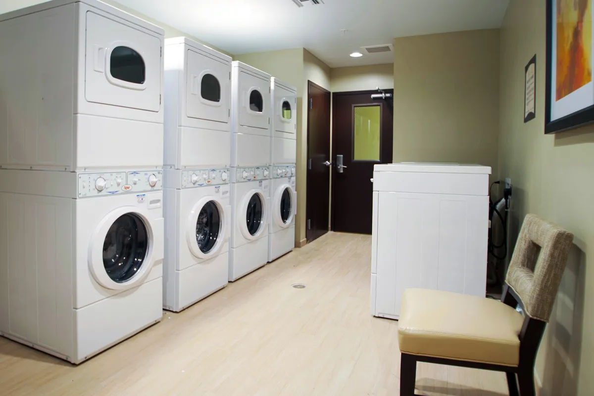 A bright and practical laundry area featuring multiple washing machines, dryer units, and comfortable bench seating. The layout suggests ease of access and thoughtful convenience for guests staying longer or with families.