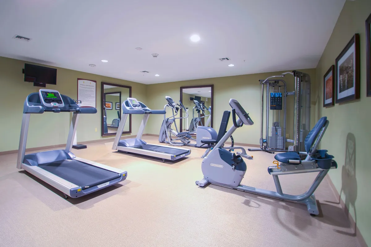 A well-equipped, brightly lit fitness center featuring treadmills, an elliptical machine, a stationary bike, and a weight machine. The room has a clean, modern look with ample space for both cardiovascular and strength training activities. Several guests are engaged in individual workouts, creating an energetic and communal atmosphere.