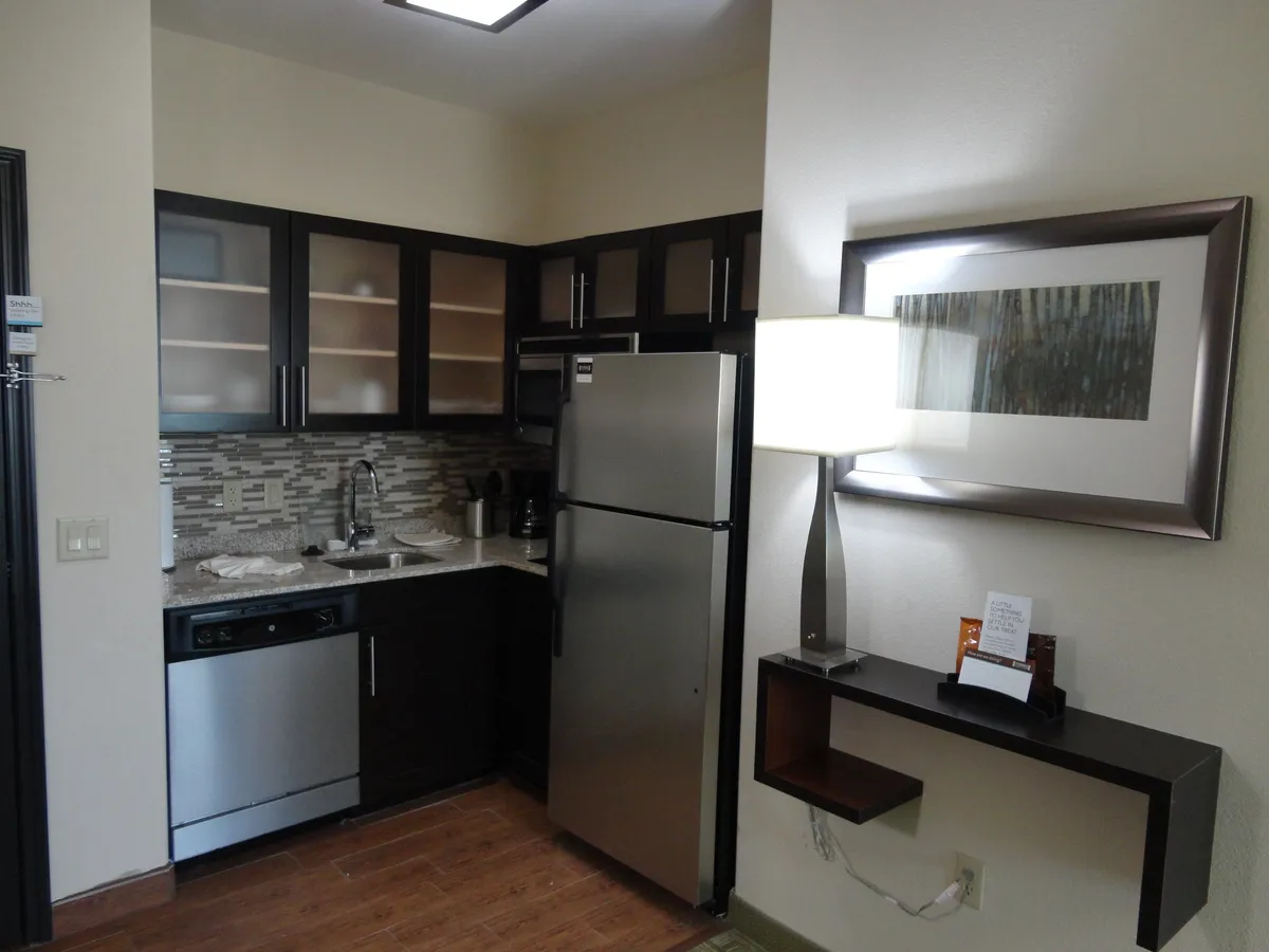A modern kitchen with stainless steel appliances, sleek cabinetry, decorative wall art, and a softly lit ambiance. Key features visible include a full-size refrigerator, stove, microwave, and a coffee maker on the countertop—conveying a home-like, fully equipped space suited for a range of meal preparations.