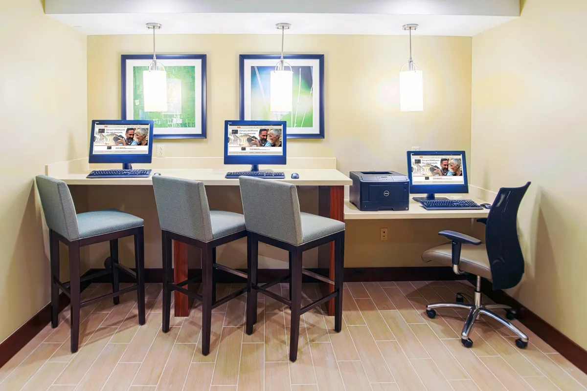 A contemporary, work-friendly area with computers set up on a counter, bar stools for casual seating, and artistic wall decor. The space is both professional and inviting, suggesting a conducive environment for productivity or casual tech use.